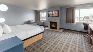 Quarto de hotel com cama, escrivaninha, cadeira, lareira e uma janela grande.