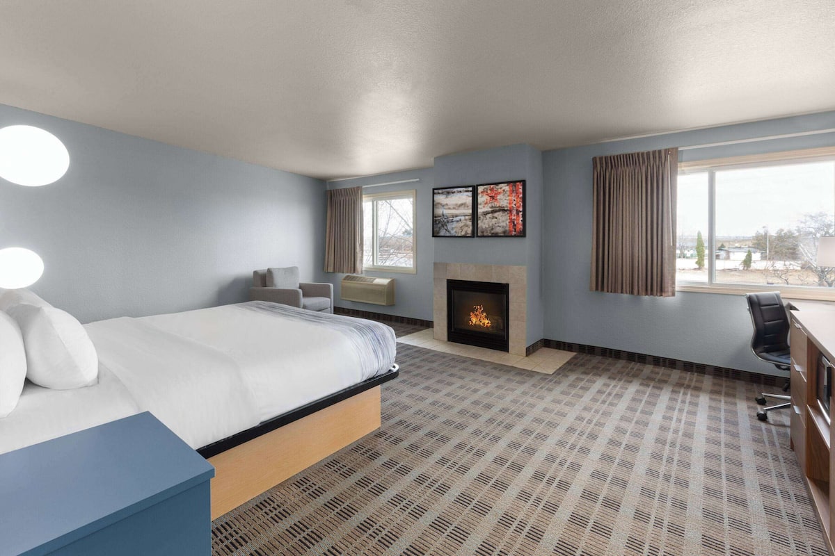 A hotel room with a bed, a desk, a chair, a fireplace, and a large window.