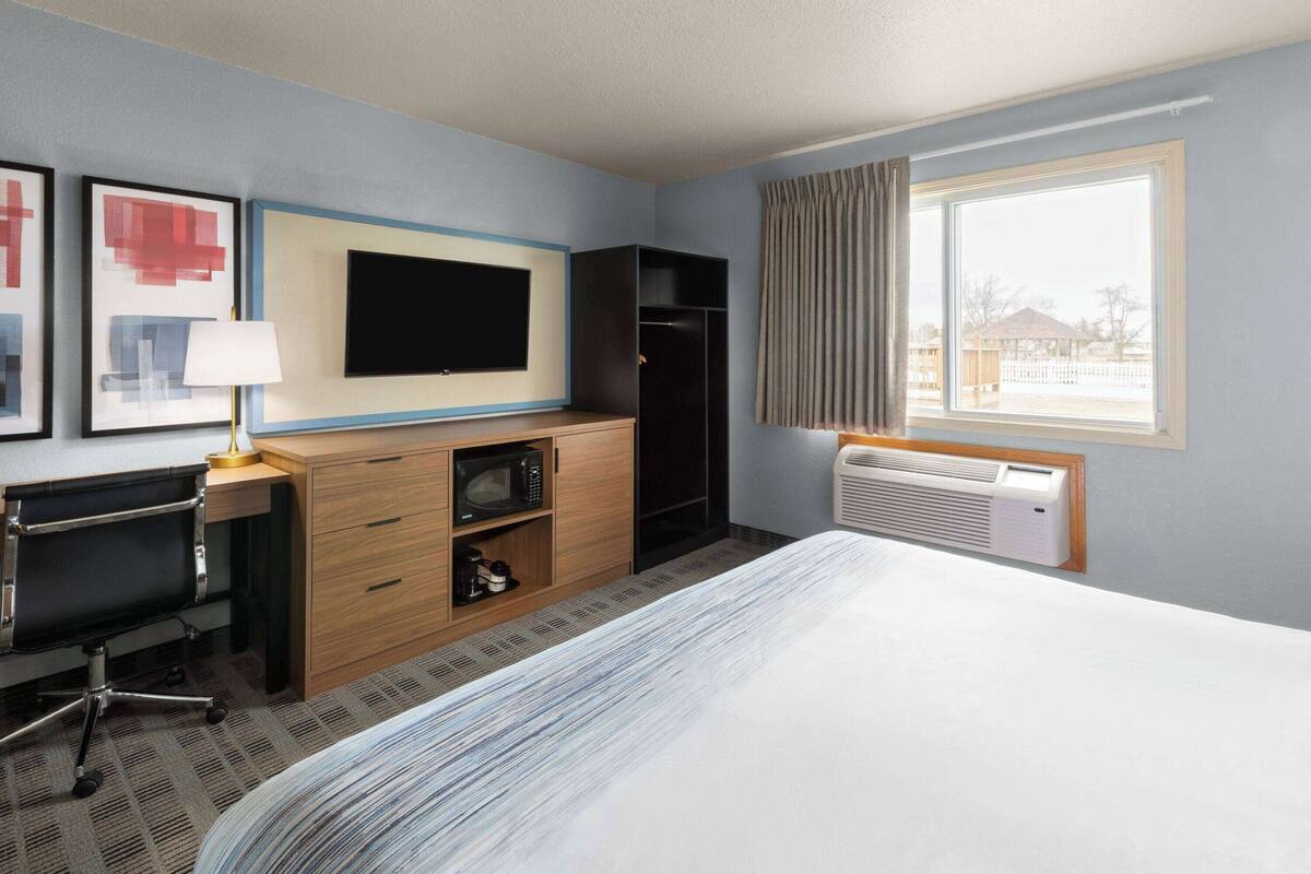 A hotel room with a bed, a desk with a chair, a TV, a wardrobe, and a window with curtains.