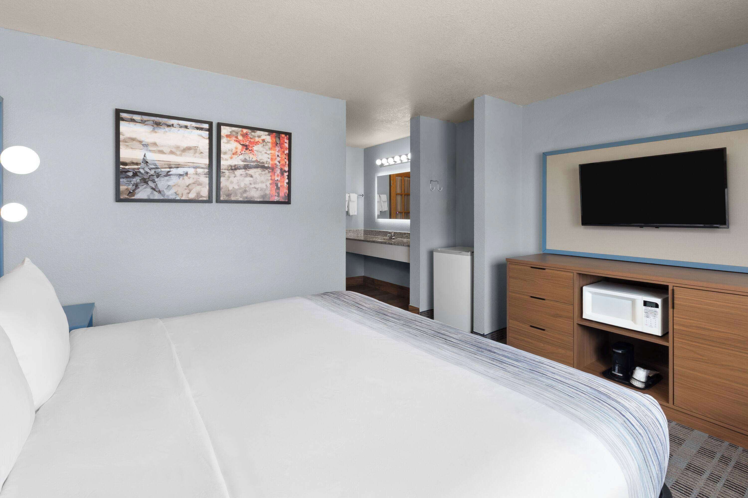 A hotel room with a large bed, a flat-screen TV mounted on the wall, a microwave, and a small coffee maker.