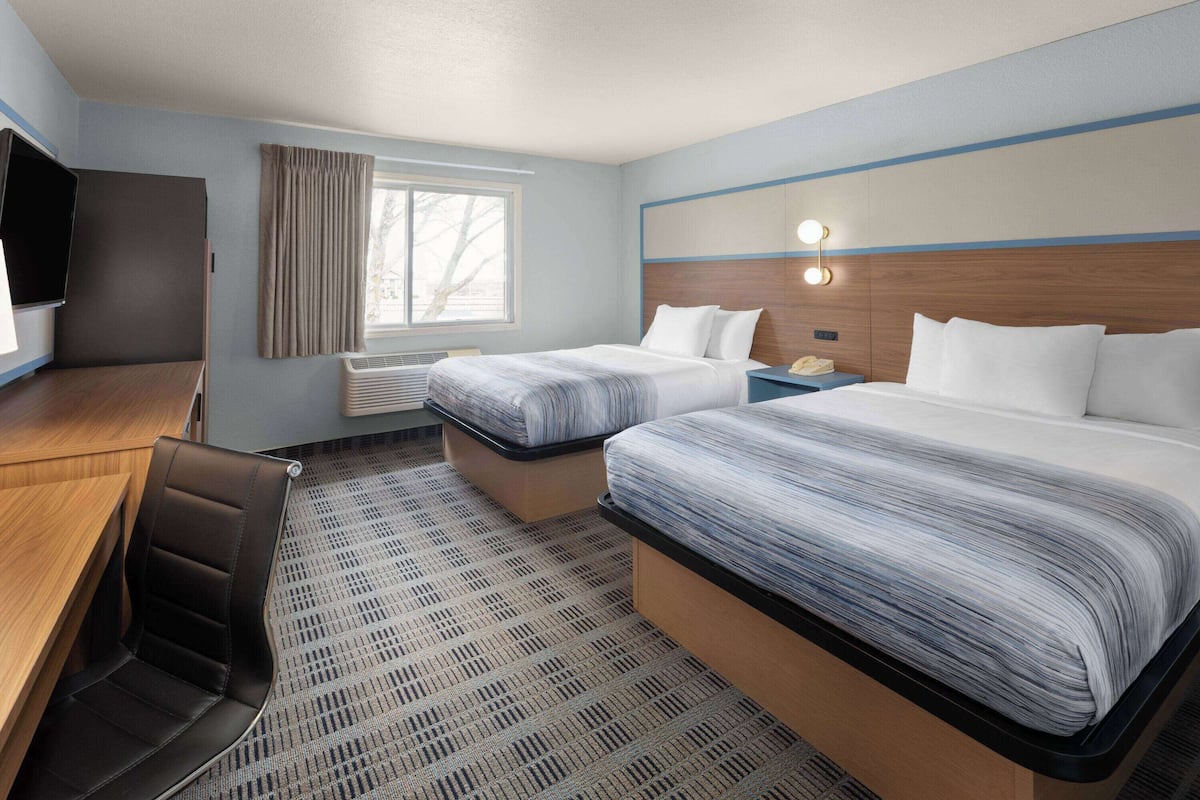 A hotel room with two beds, a desk, a chair, a TV, and a window with curtains.