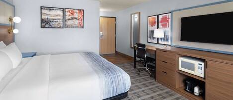 A hotel room with a bed, desk, chair, TV, and microwave.