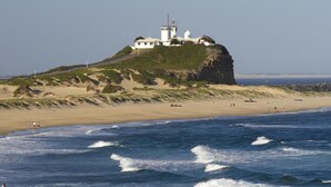 En kystbygning med et fyrtårn på en klippe, med udsigt over en sandstrand og havet.