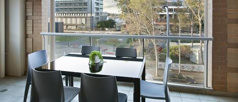A modern room with a balcony, a dining table with chairs, and a view of buildings and trees.