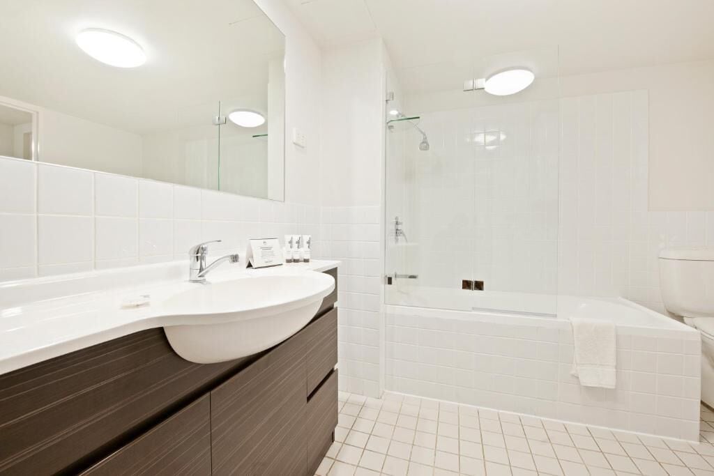 Ein modernes Badezimmer mit Waschbecken in Weiß, dunklem Holzschrank und einer Duschkabine aus Glas. Eine weiße Badewanne ist ebenfalls vorhanden.