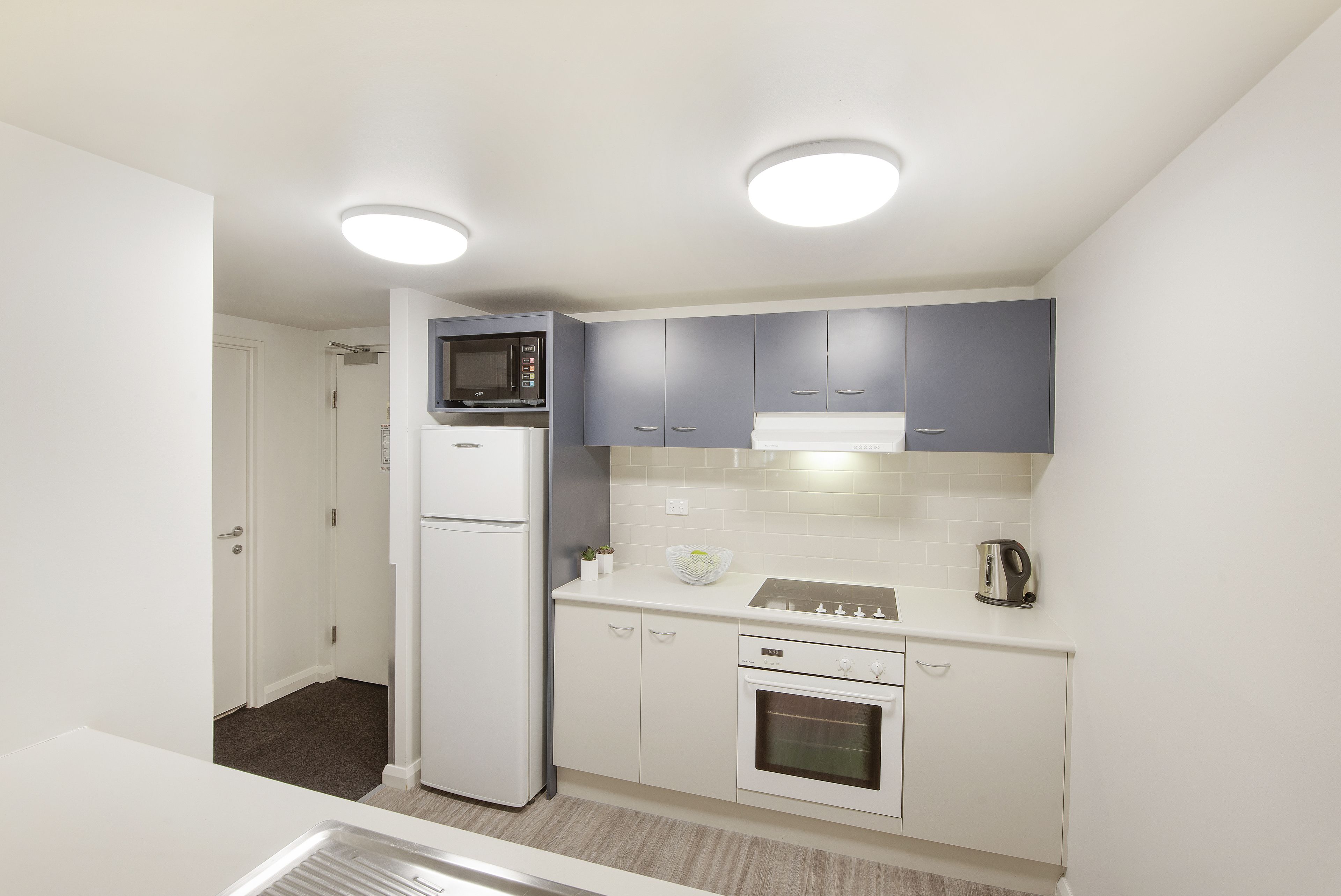 Una cocina funcional con electrodomésticos blancos, armarios grises y dos luces en el techo.