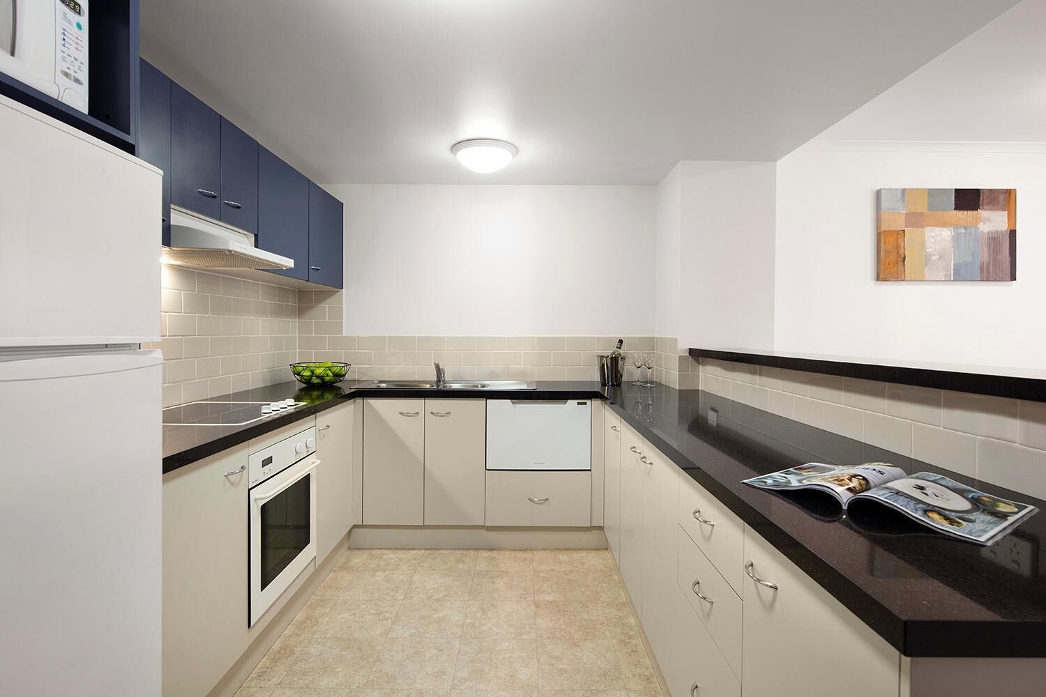Una cocina moderna con armarios blancos, encimera negra y salpicadero de azulejos.