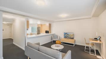 Una sala de estar moderna con un sofá gris, una mesa de centro redonda, una mesita auxiliar de madera y un televisor sobre un mueble de madera.
