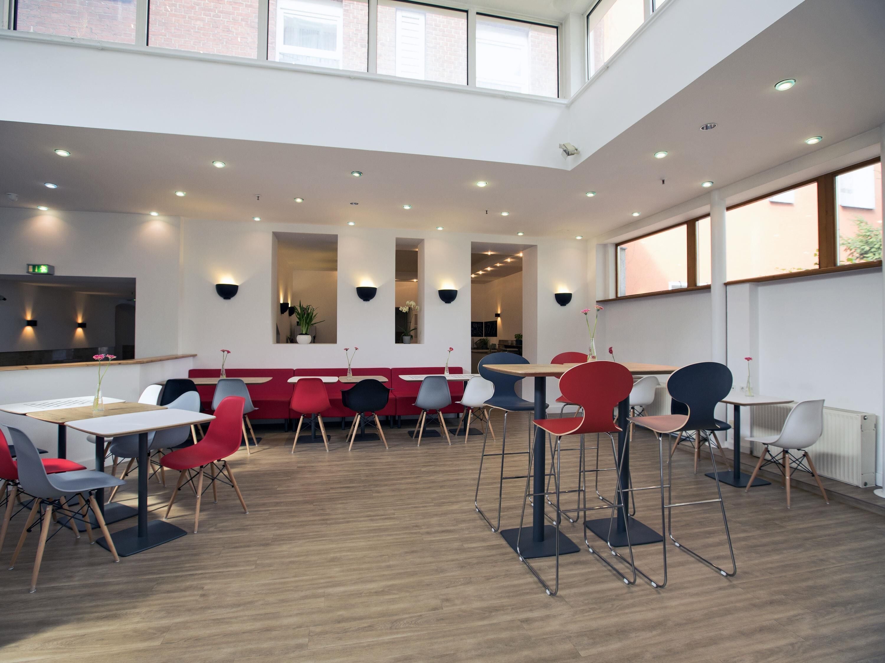 A modern interior with high ceilings, recessed lighting, and a mix of red and grey seating.