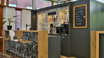 Uma área de bar moderna com cardápio em lousa, banquetas, máquina de café e um vaso de planta.