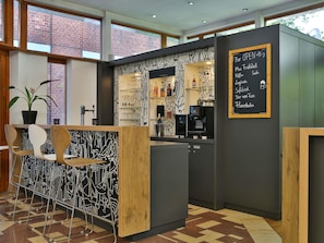 Un área de bar moderna con un menú en una pizarra, taburetes, una máquina de café y una planta en maceta.