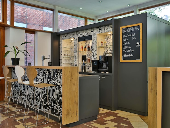 Un área de bar moderna con un menú en una pizarra, taburetes, una máquina de café y una planta en maceta.