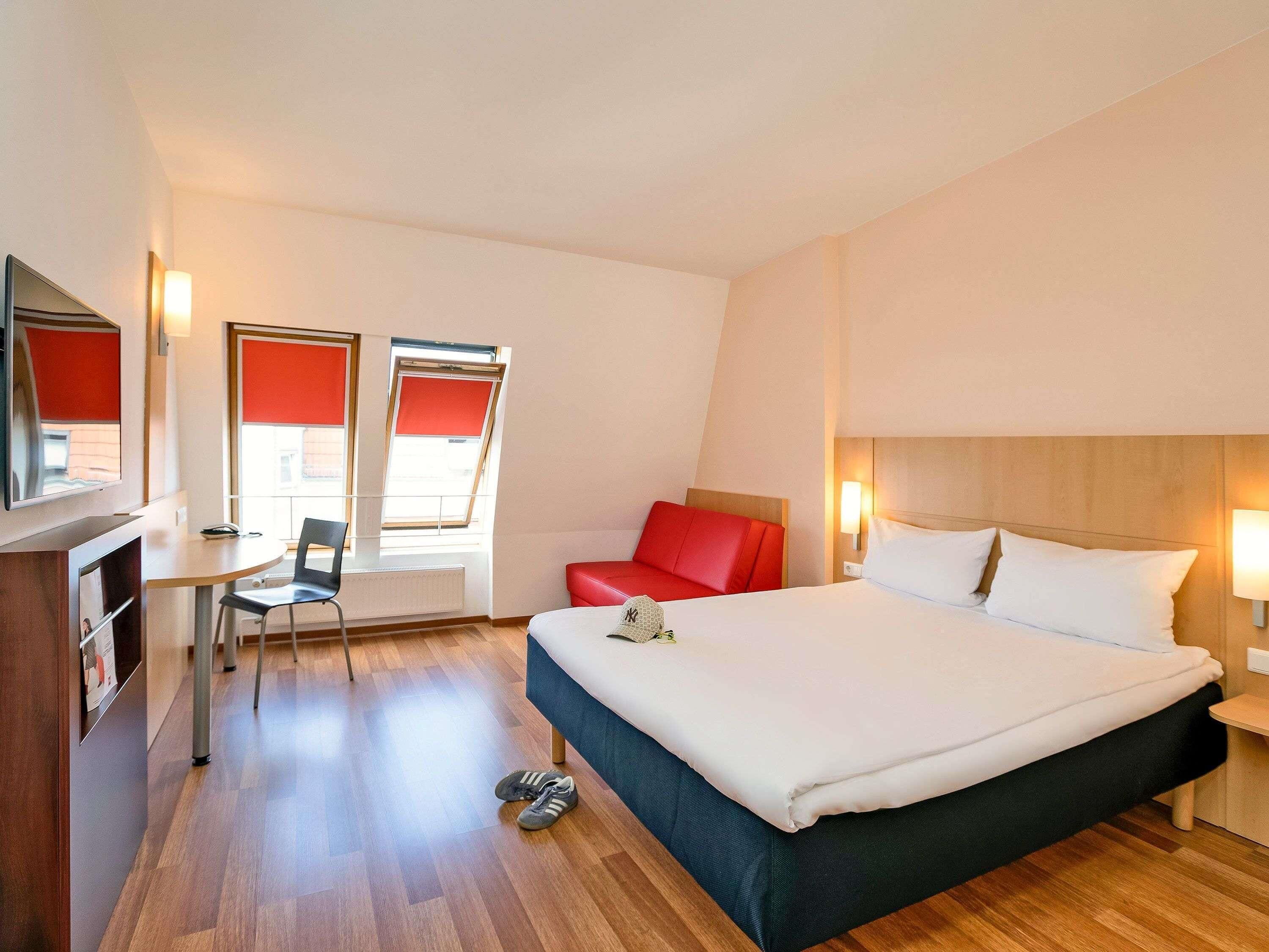 A hotel room with a bed, a desk, a chair, and a TV.