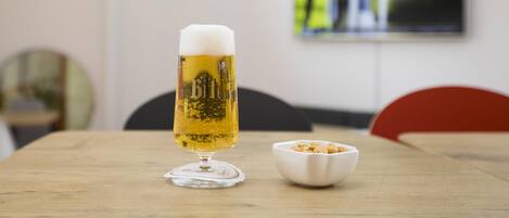 A beer glass on a wooden table with a bowl of peanuts beside it.