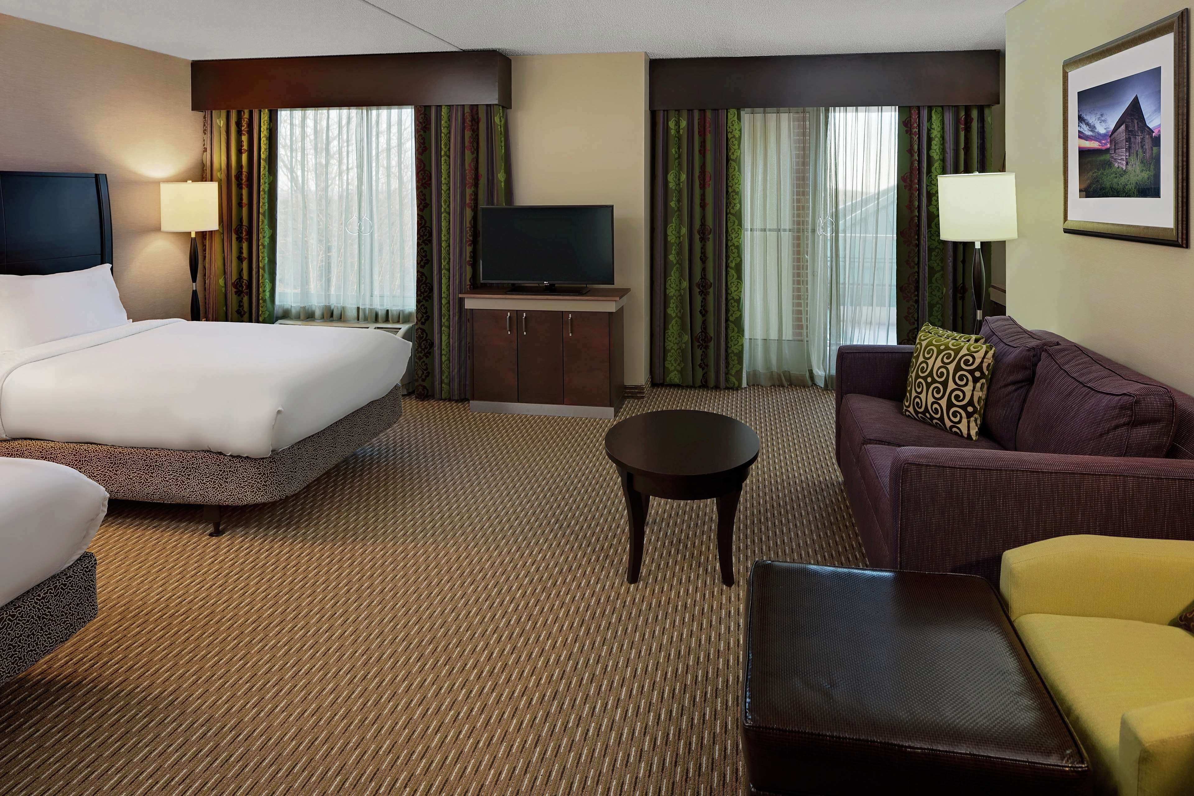 A hotel room with a bed, a sofa, a small table, a television on a cabinet, and curtains.