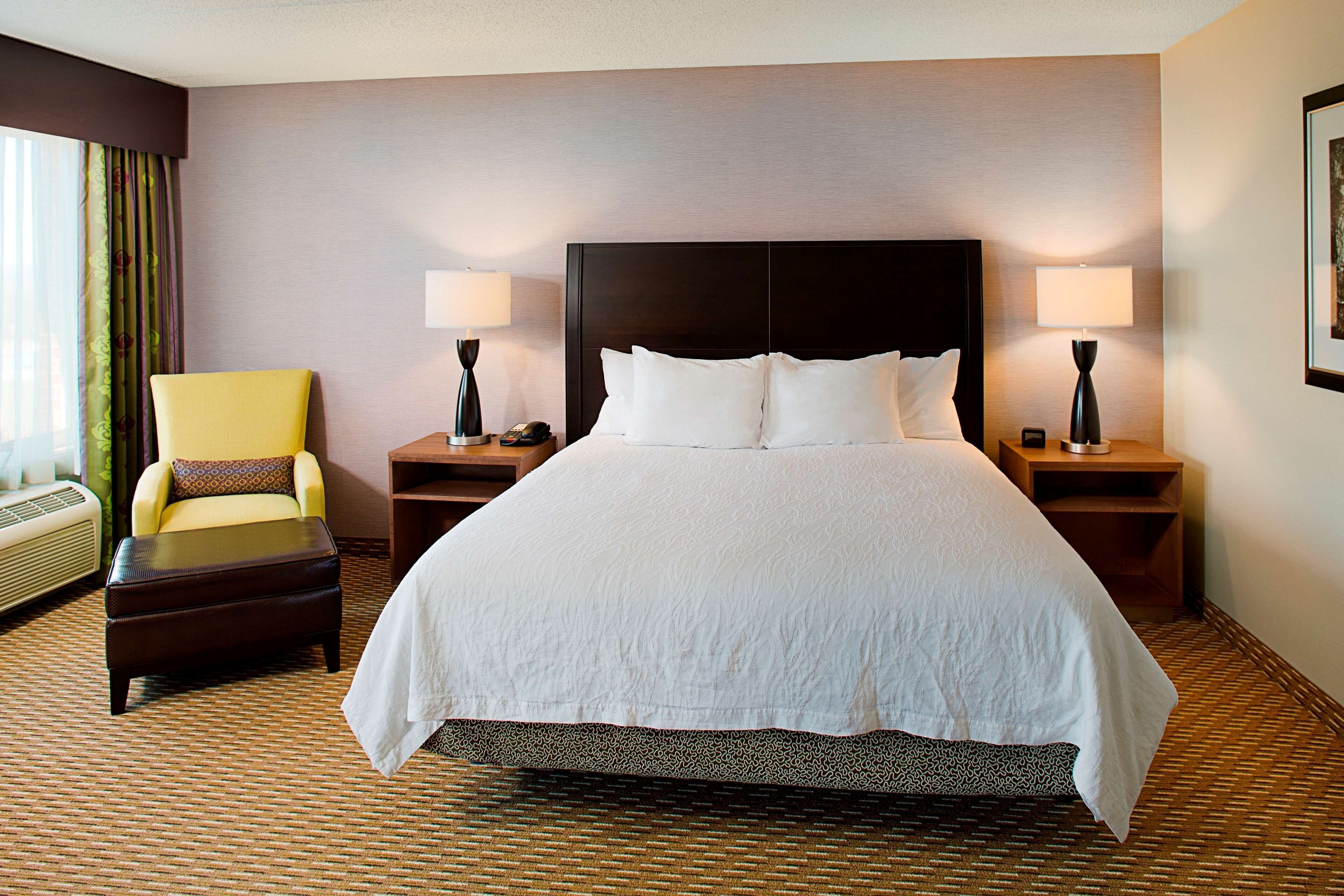 Une chambre d’hôtel avec un grand lit, deux tables de chevet avec des lampes, une chaise et une vue sur l’extérieur.