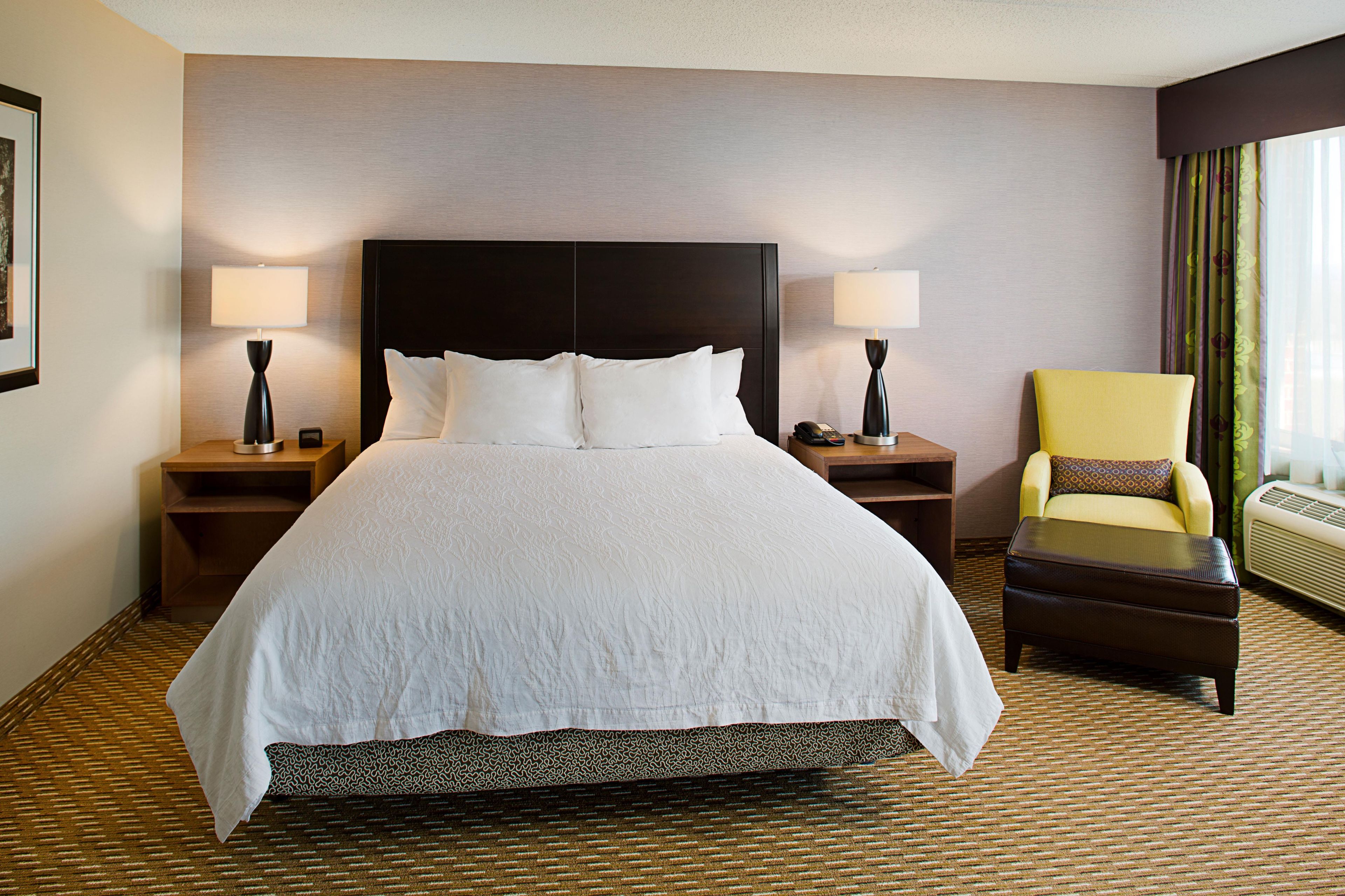 A hotel room with a large bed, two bedside tables, a chair, and a window with curtains.