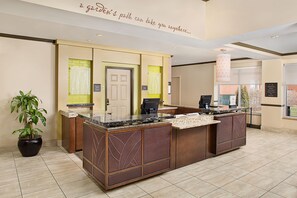A reception desk with a check-in counter, a potted plant, and a wall with directional signs.