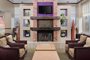 A modern living room with a fireplace, comfortable seating, and a flat-screen TV mounted above the fireplace. - Hilton Garden Inn Hartford North/Bradley Int'l Airport (Windsor)