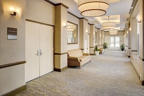 A hotel corridor with a sofa, potted plants, and a sign indicating room number.