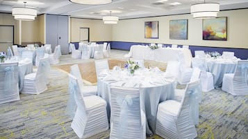 A banquet hall with round tables, white tablecloths, and chairs with white covers.