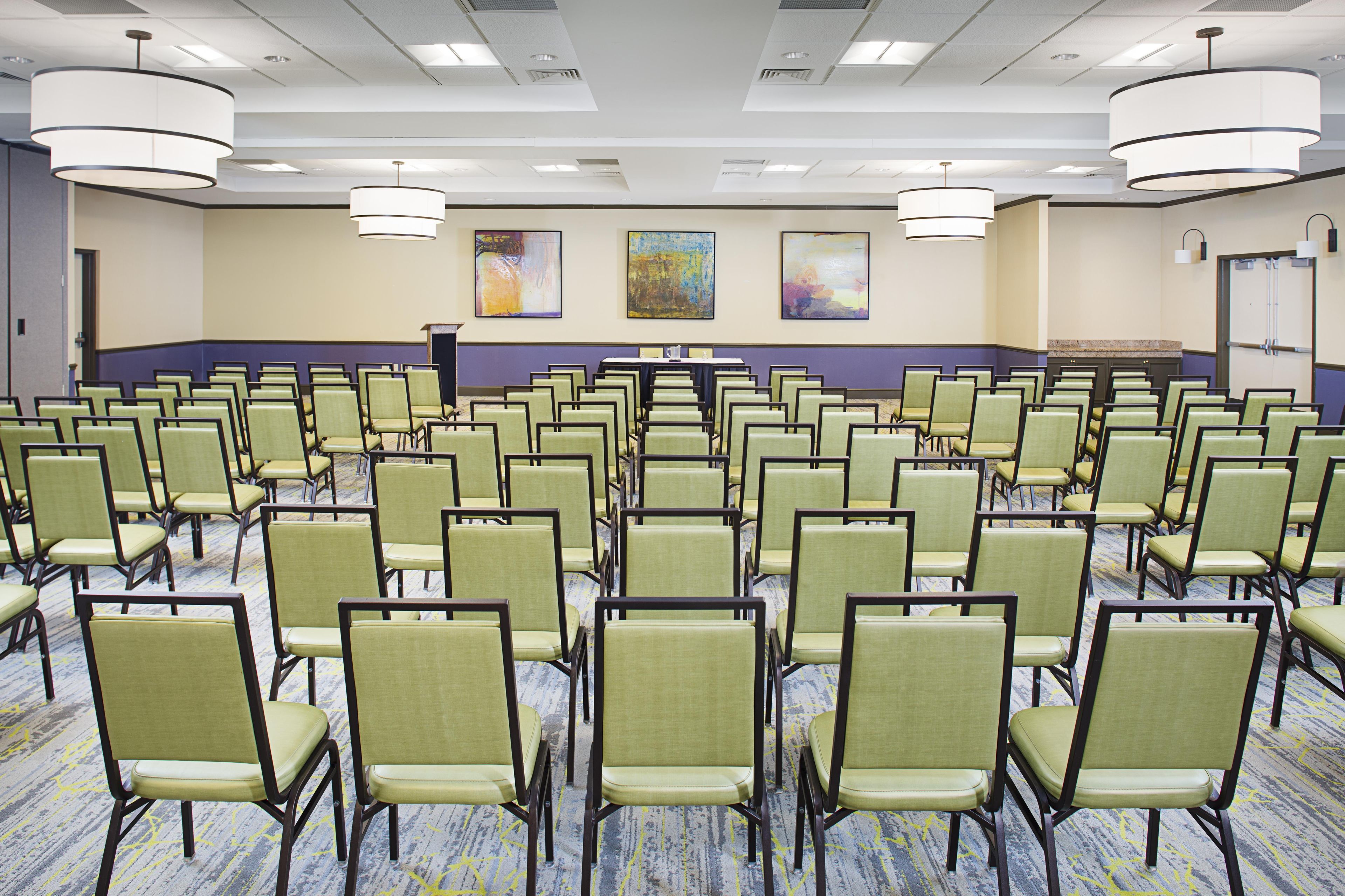 A conference room with rows of chairs, a podium, and abstract paintings on the wall.