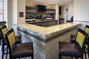 A bar area with a granite countertop, multiple liquor bottles, a television, and bar stools.
