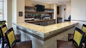 A bar area with a granite countertop, bar stools, and a television above the bar.