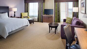 A hotel room with a bed, a sofa, a desk, a television, and a window with curtains.