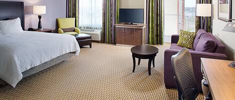 A hotel room with a bed, a sofa, a desk, a television, and a window with curtains.