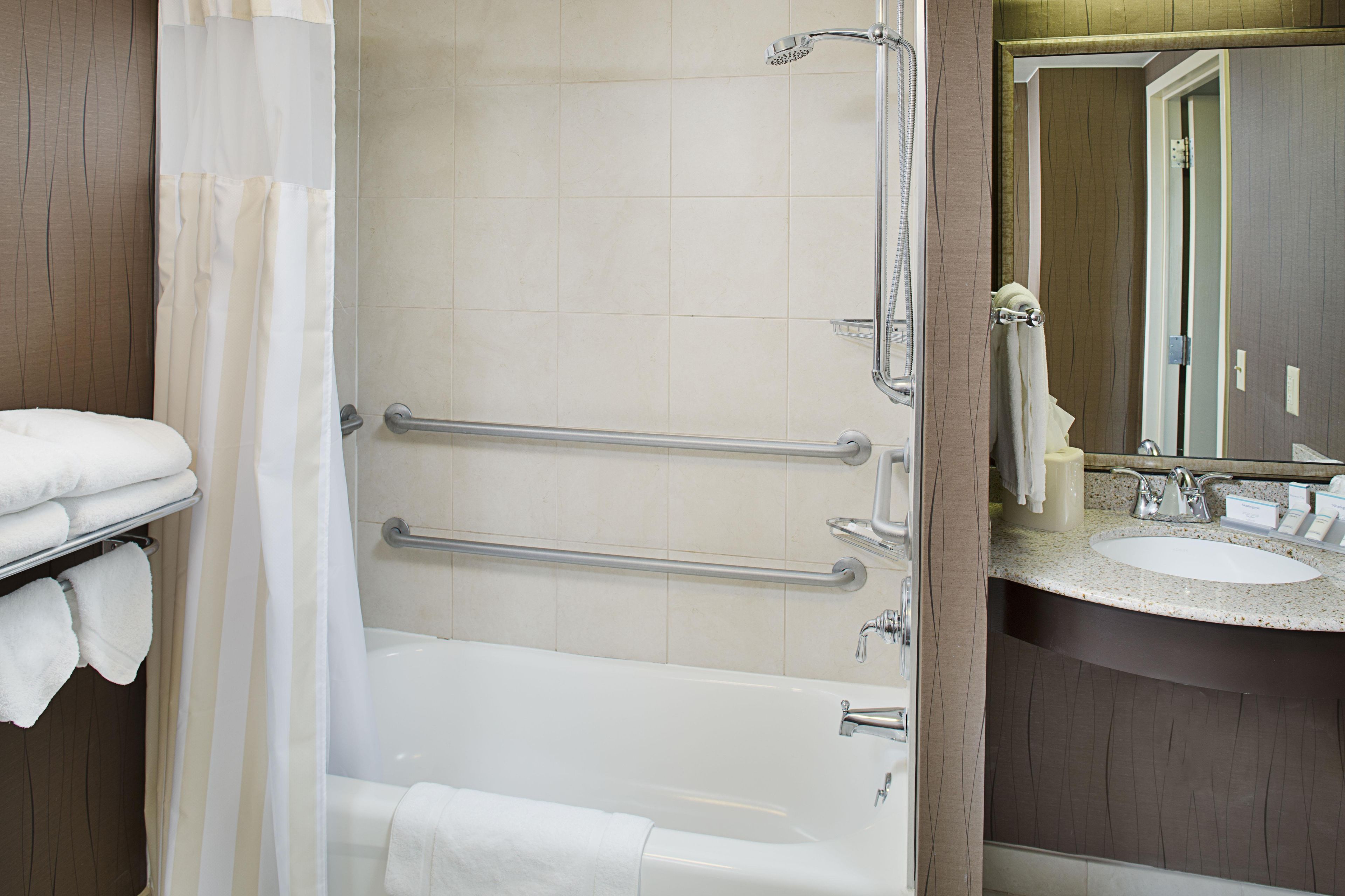A bathroom with a bathtub, a shower, and a sink with a mirror. There are grab bars installed for safety.
