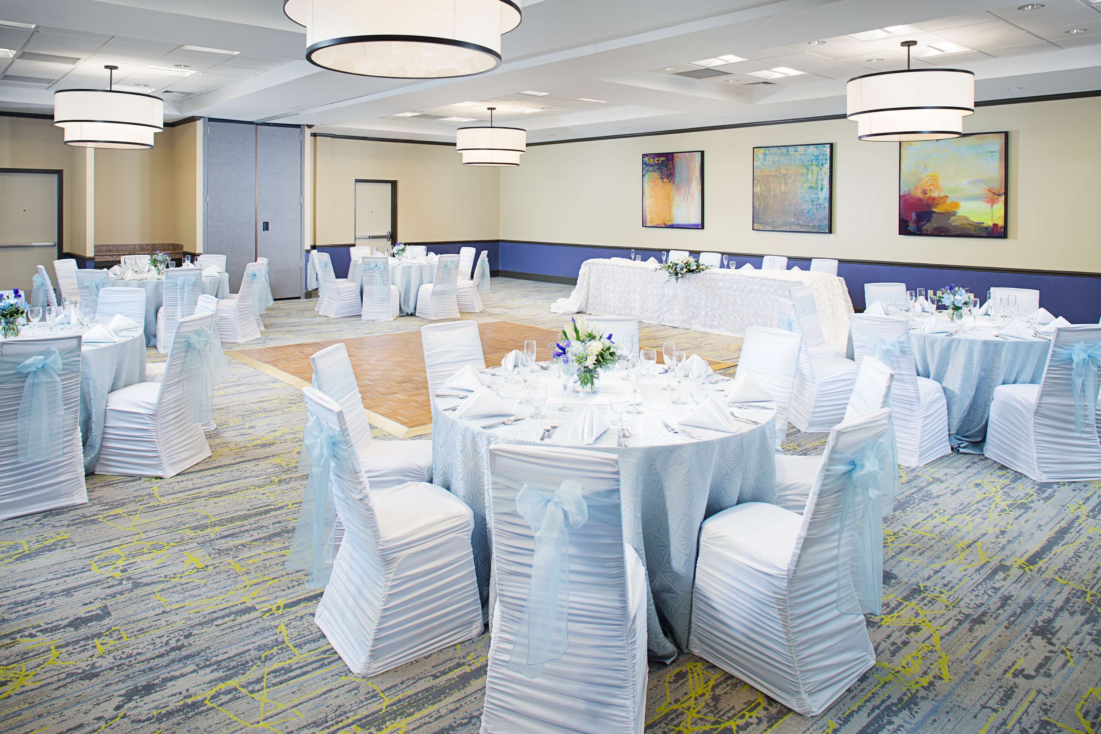 A banquet hall with round tables, white chairs, and chandeliers.