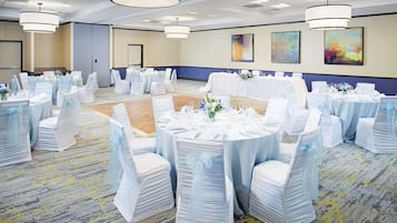 A banquet hall with round tables, white chairs, and chandeliers.