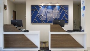 Un comptoir d’accueil doté de deux écrans d’ordinateur, d’un élément de décoration murale aux motifs géométriques bleus et d’une enseigne indiquant « Holiday Inn Express & Suites ».