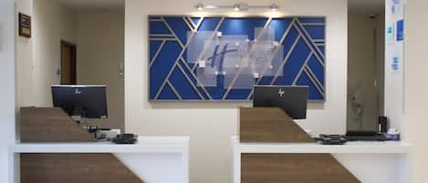 A reception desk with two computer monitors, a blue geometric wall decoration, and a sign for Holiday Inn Express & Suites.