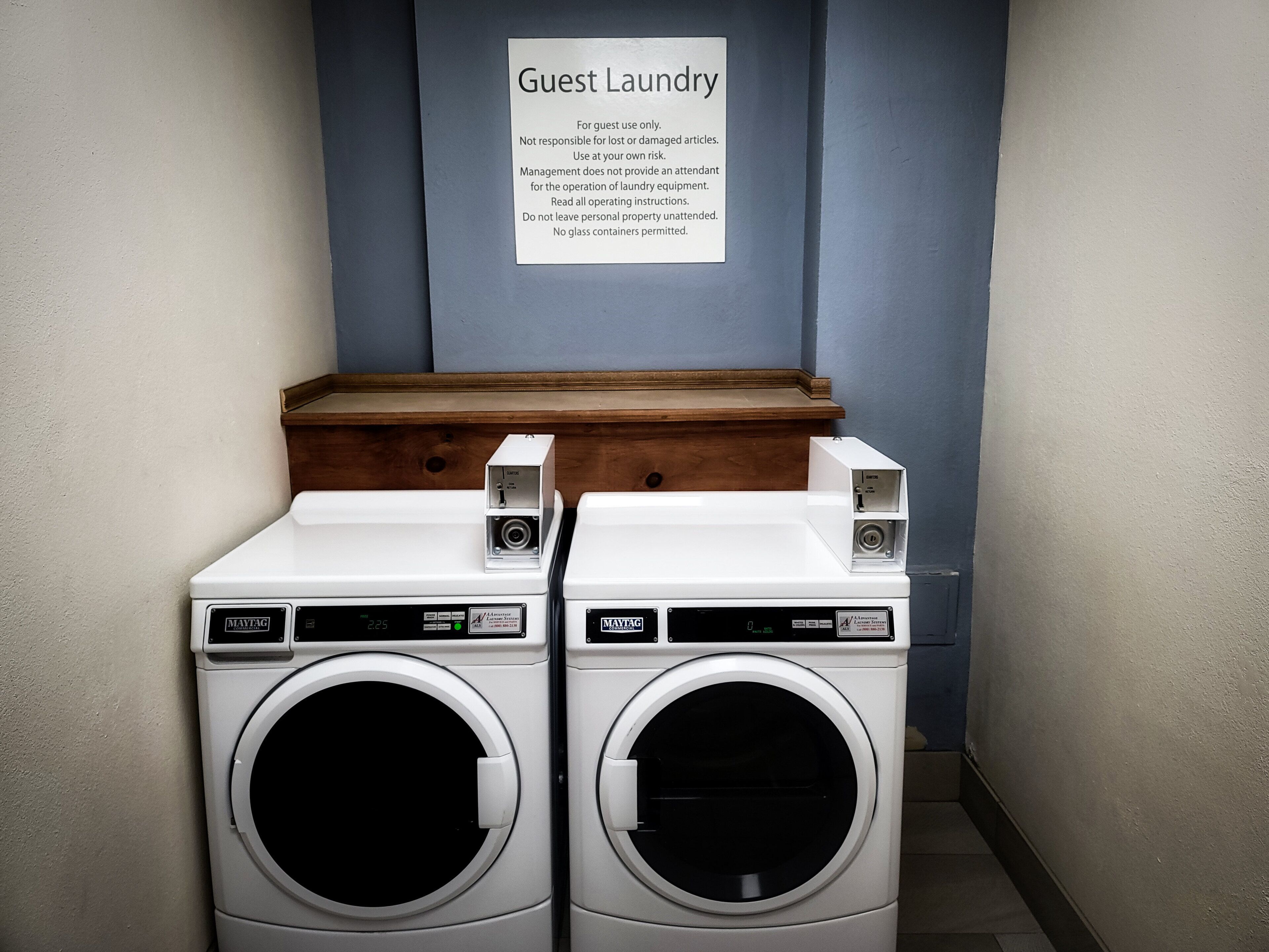 Un área de lavandería para huéspedes con dos lavadoras Maytag, un banco de madera y un letrero con instrucciones para el uso de la lavandería.