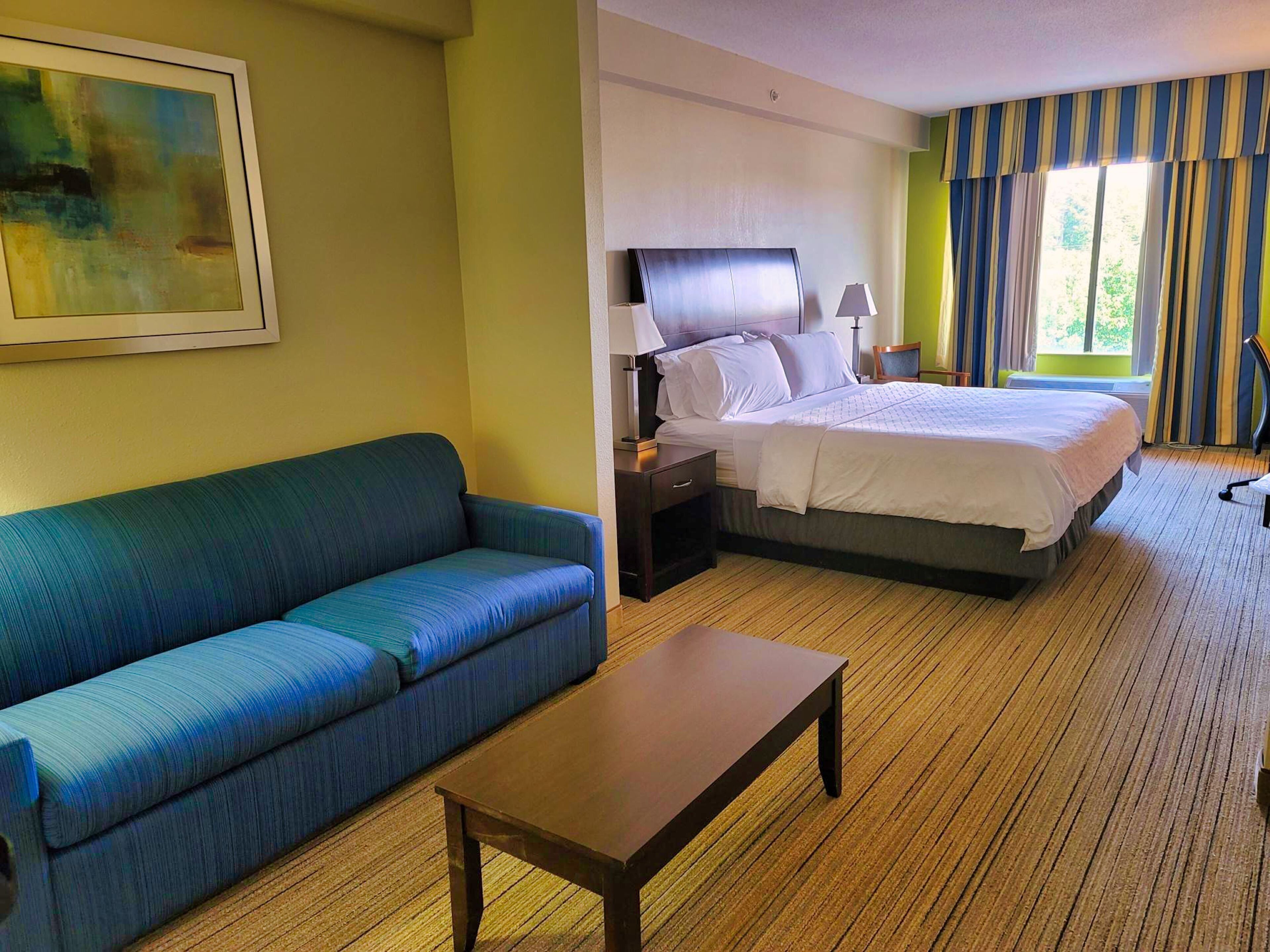 Habitación de hotel con cama, sofá, mesita de noche, lámpara y un cuadro en la pared.