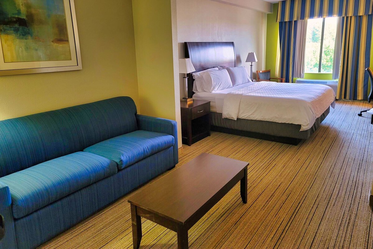 Habitación de hotel con cama, sofá azul, mesa de madera y un cuadro en la pared.