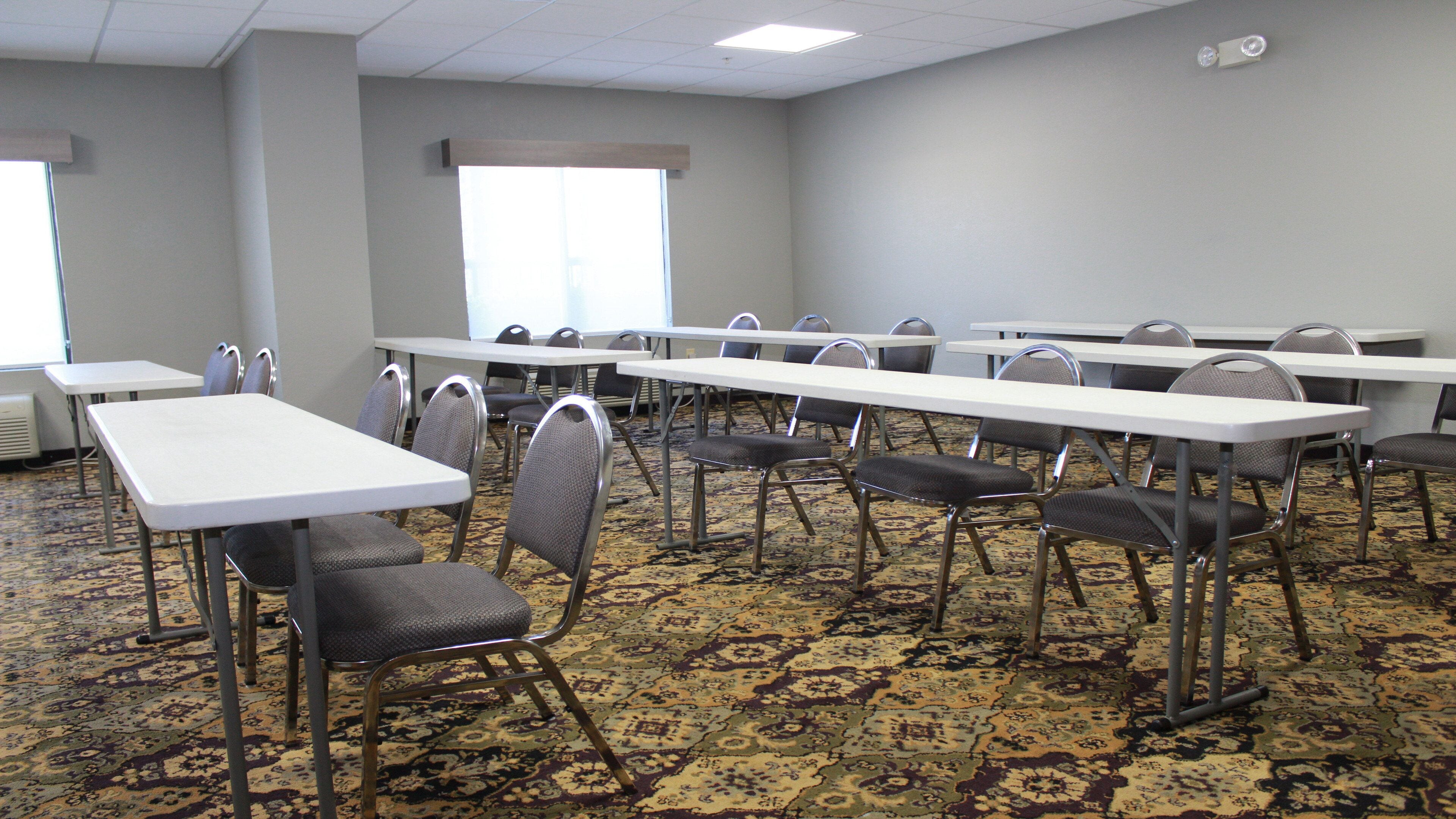 A conference room with multiple tables and chairs, carpeted floor, and large windows.