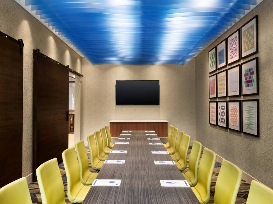 A conference room with a long table, yellow chairs, a flat-screen TV, and framed artwork on the walls.