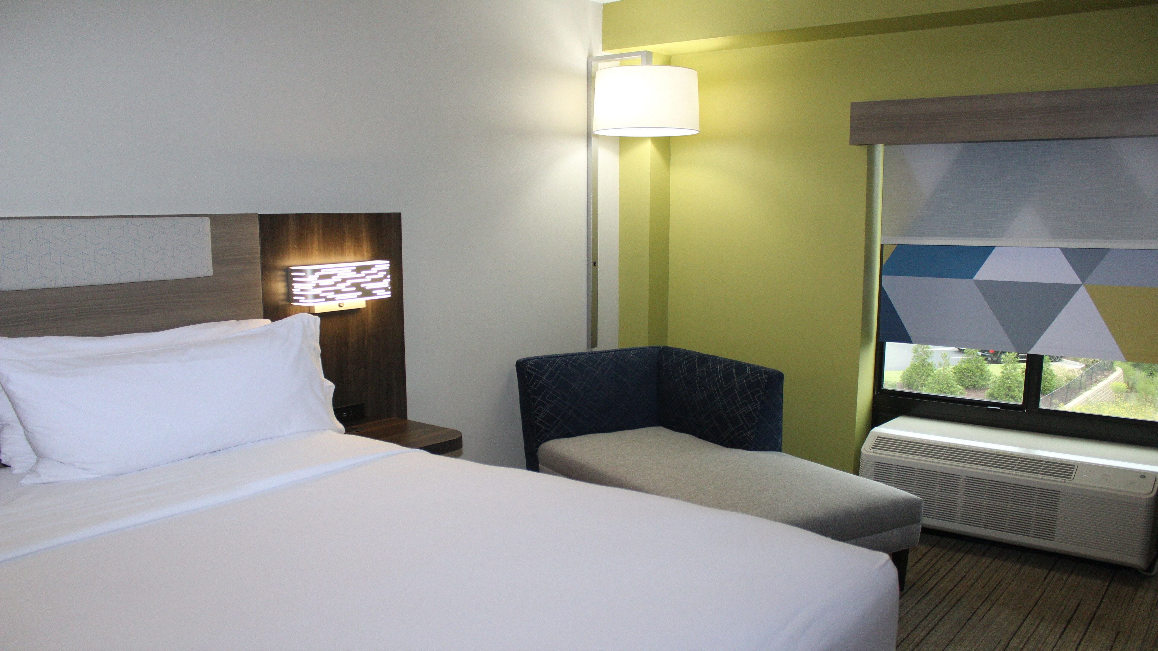 A hotel room with a bed, a chair, a lamp, and a window with a view.