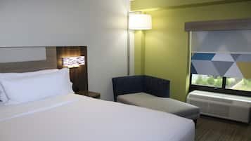 A hotel room with a bed, a chair, a lamp, and a window with a view.