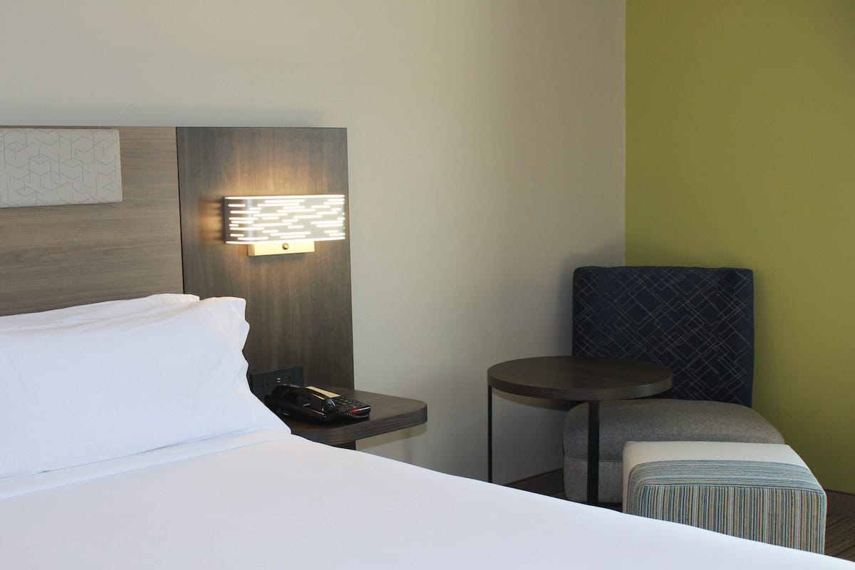 A hotel room with a bed, a bedside table with a phone, a small table, and a chair.