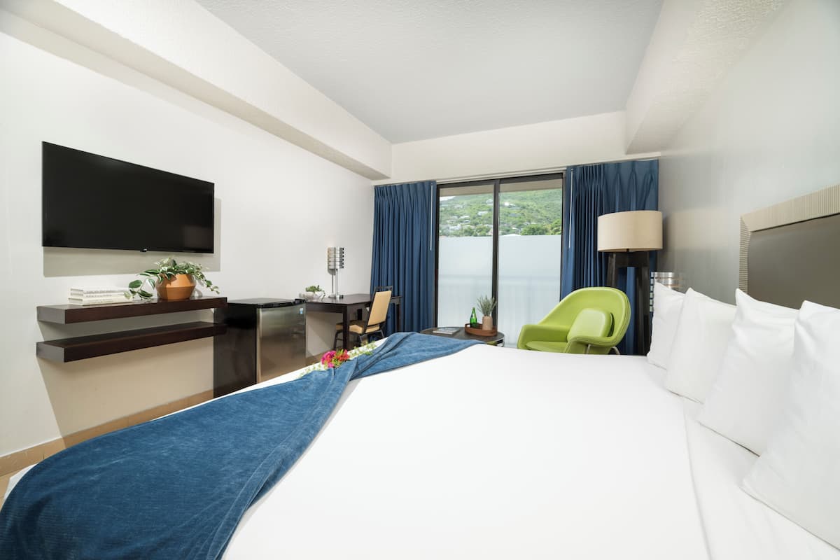 Ein Hotelzimmer mit Bett, Schreibtisch, Stuhl, Fernseher und einem Fenster mit Vorhängen.