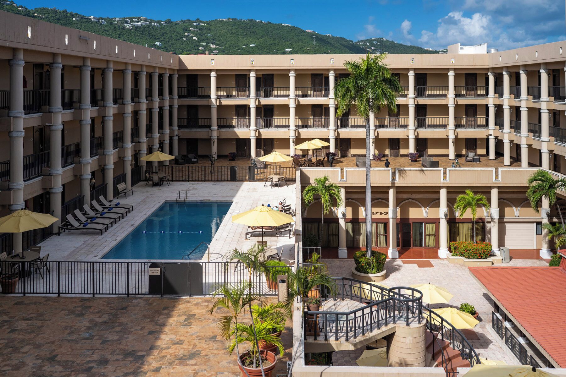 A hotel with a central pool, multiple balconies, and outdoor seating areas.