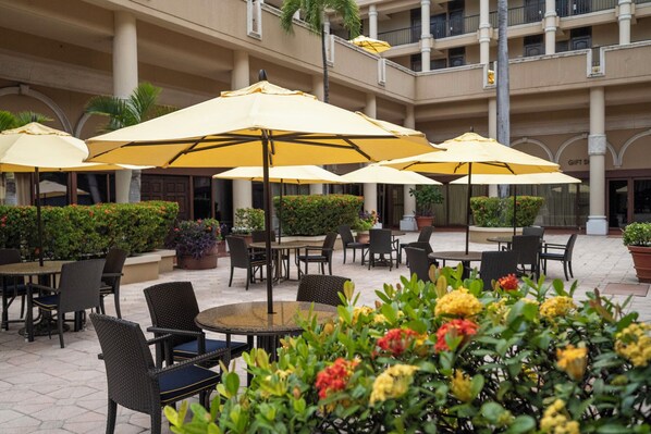 An outdoor patio area with multiple round tables and chairs, surrounded by yellow umbrellas.