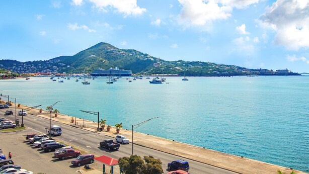 A coastal road with parked cars, a marina with boats, and a mountain in the background. - Windward Passage Hotel (St. Thomas)