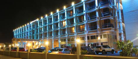 A multi-story hotel with balconies, a parking area, and a well-lit facade.