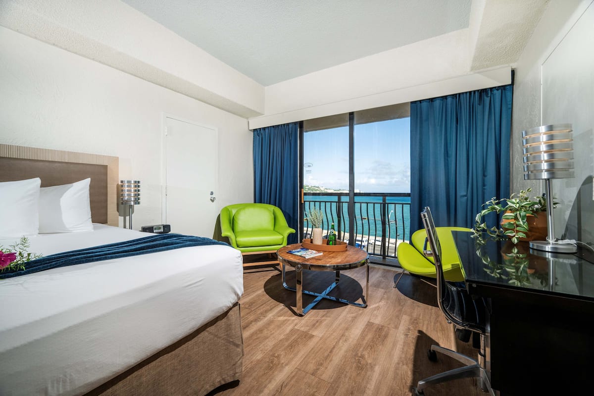 Ein Hotelzimmer mit einem Bett, zwei Stühlen, einem Schreibtisch und einem Balkon mit Blick.