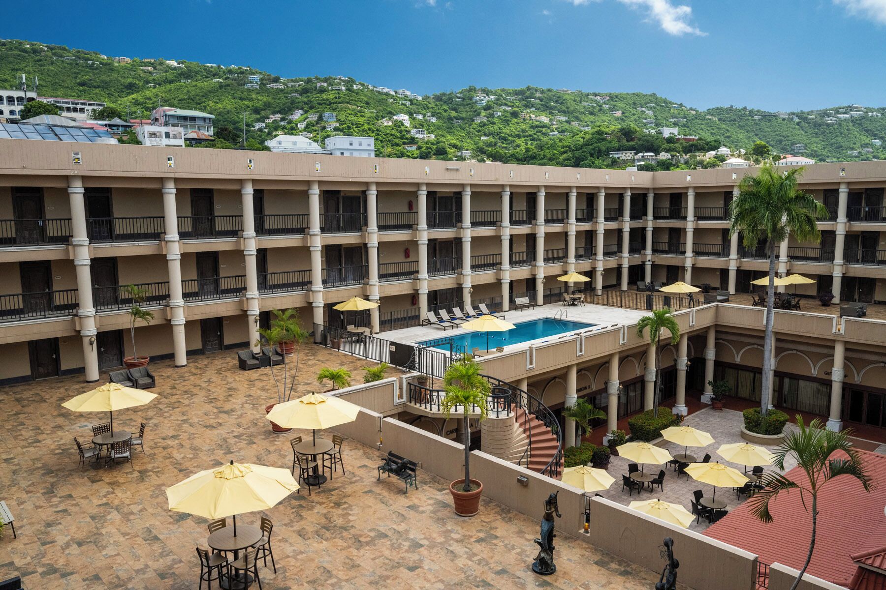 A multi-story hotel with a central swimming pool surrounded by outdoor seating areas with umbrellas.